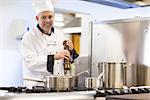 Smiling head chef flavoring food with pepper in professional kitchen