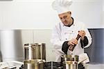 Focused head chef using pepper mill in professional kitchen