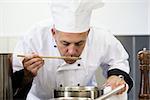 Focused head chef tasting sauce with wooden spoon in professional kitchen