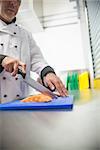 Chef cutting raw salmon with sharp knife in professional kitchen