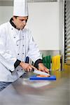 Serious chef cutting raw salmon with knife on blue cutting board in professional kitchen