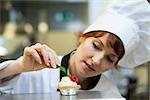 Focused head chef putting mint leaf on little cake in professional kitchen