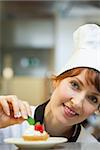 Smiling head chef putting mint leaf on little cake in professional kitchen