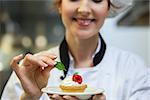 Smiling head chef putting mint leaf on little cake on plate in professional kitchen