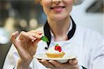 Happy head chef putting mint leaf on little cake on plate in professional kitchen