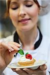 Focused head chef putting mint leaf on little cake on plate in professional kitchen
