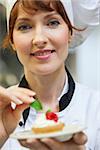 Gorgeous head chef putting mint leaf on little cake on plate in professional kitchen