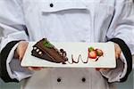 Chef presenting chocolate cake with strawberries on white plate