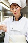 Pretty concentrating head chef finishing a cake with icing in professional kitchen