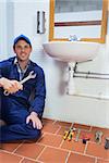 Cheerful plumber holding wrench sitting next to sink in public bathroom