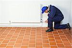 Handyman in blue boiler suit repairing a radiator in bright room