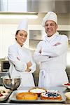 Smiling chef and head chef standing arms crossed looking at camera