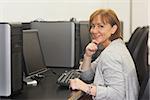 Cheerful female mature student sitting in computer class smiling at camera