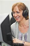 Happy mature woman working on computer while listening to music