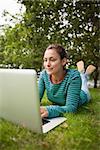 Casual student lying on grass using laptop on campus at college