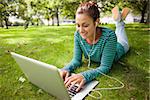 Smiling casual student lying on grass using laptop on campus at college