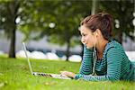 Attractive casual student lying on grass using laptop on campus at college