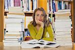 Exhausted pretty student studying between piles of books in library
