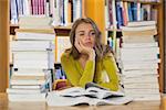 Thoughtful pretty student studying between piles of books in library