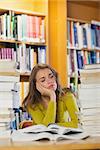 Exhausted beautiful student studying between piles of books in library