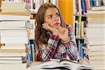 Serious pretty student sitting between piles of books in library