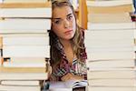 Stern pretty student studying between piles of books in library