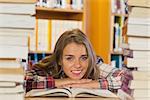 Smiling pretty student studying between piles of books in library