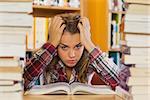 Annoyed pretty student studying between piles of books in library