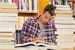 Focused handsome student studying between piles of books in library