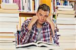 Irritated handsome student studying between piles of books in library