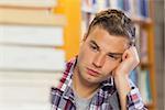 Exhausted handsome student studying between piles of books in library