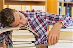 Tired handsome student resting head on piles of books in library