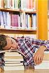 Exhausted handsome student resting head on piles of books in library