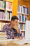 Handsome thoughtful student using computer in library