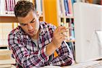 Handsome serious student pointing at computer in library