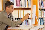 Handsome focused student pointing at computer in library