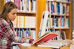 Pretty focused student reading book using computer in library