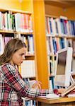 Pretty concentrating student reading book using computer in library