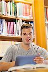 Attractive smiling student using tablet in library