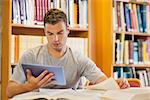 Attractive focused student using tablet and turning page in library