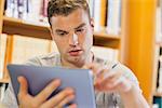Attractive serious student using tablet in library