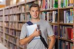 Handsome smiling student holding tablet in library