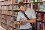 Handsome unsmiling student looking at tablet in library