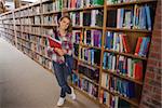 Pretty smiling student holding notebooks in library