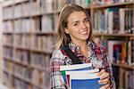 Pretty smiling student holding books in library