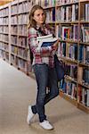 Pretty smiling student looking at camera holding books in library