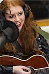 Beautiful singer recording and playing guitar in studio at college