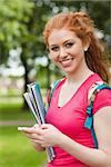 Gorgeous cheerful student holding notebooks texting on campus at college