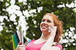 Gorgeous happy student holding notebooks phoning on campus at college