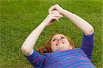 Gorgeous smiling student lying on grass texting on campus at college